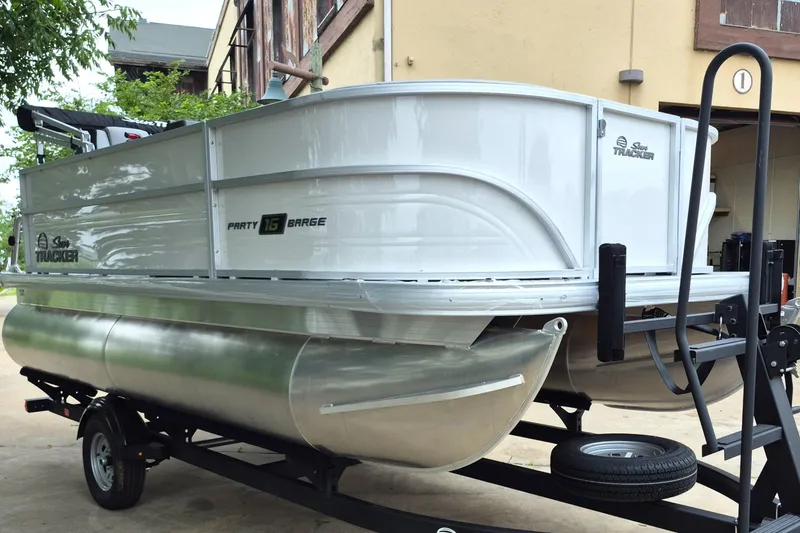 Slide: The Image of 2026 Sun Tracker Party Barge 16 DLX pontoon boat on trailer, parked outdoors. - 2