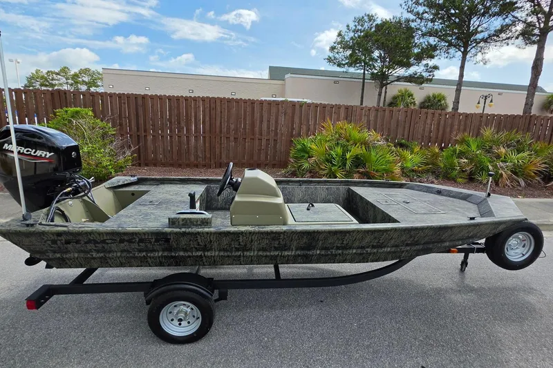 Slide: The Image of 2026 Tracker Grizzly 1648 SC boat on trailer, outdoors with trees and fence background. - 5