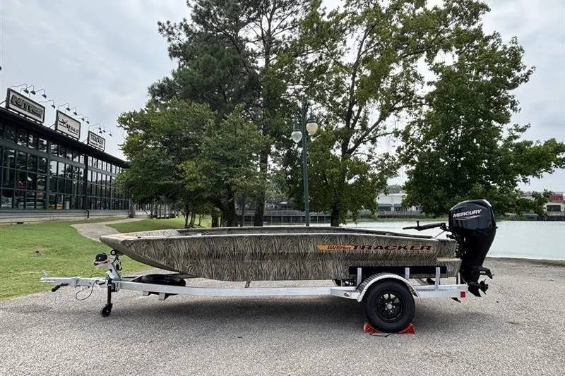 The Image of 2026 Tracker Grizzly 1756 T Marsh boat on trailer, parked near trees and a building. - 0