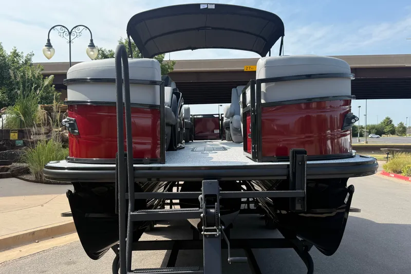 Slide: The Image of 2026 Regency 230 DL pontoon boat with red accents, parked outdoors under a clear sky. - 2