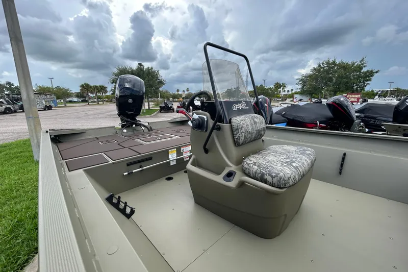 Slide: The Image of 2026 Tracker Grizzly 2072 CC boat with camouflage seating, parked outdoors under cloudy skies. - 7