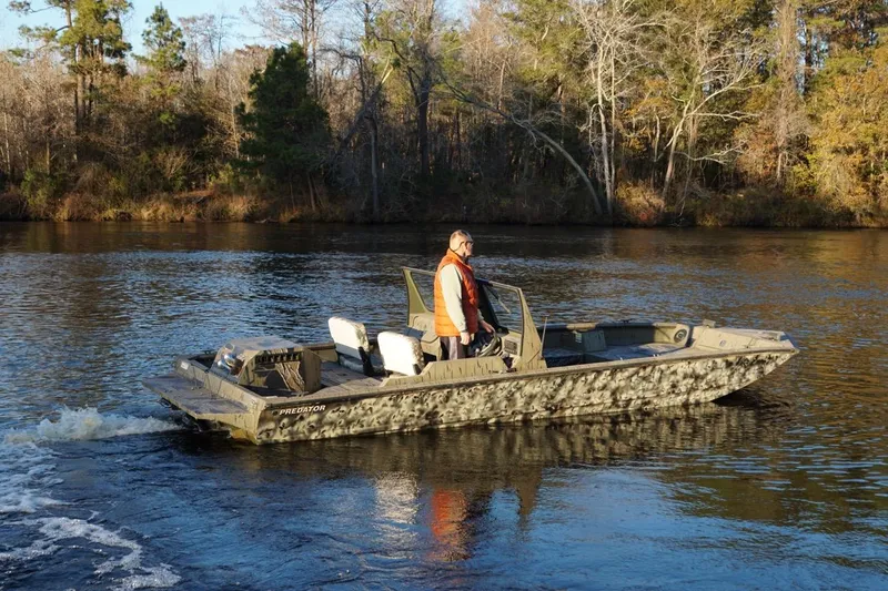 Slide: The Image of 2019 SeaArk Predator 220 AK SC boat cruising on a calm river with trees in the background. - 2