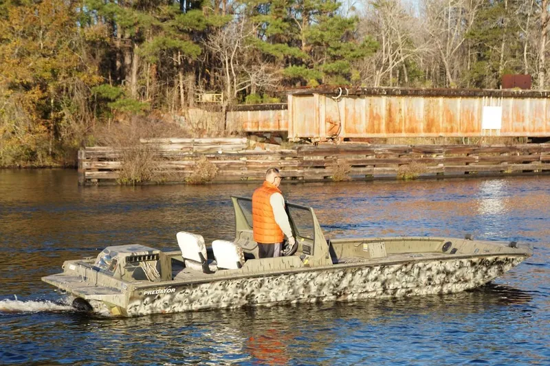 Slide: The Image of 2019 SeaArk Predator 220 AK SC boat cruising on a calm river near a wooded shoreline. - 3