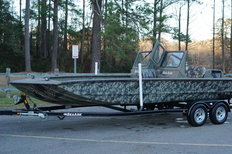 Slide: The Image of 2019 SeaArk Predator 220 AK SC boat on trailer, camo design, parked in wooded area. - 5