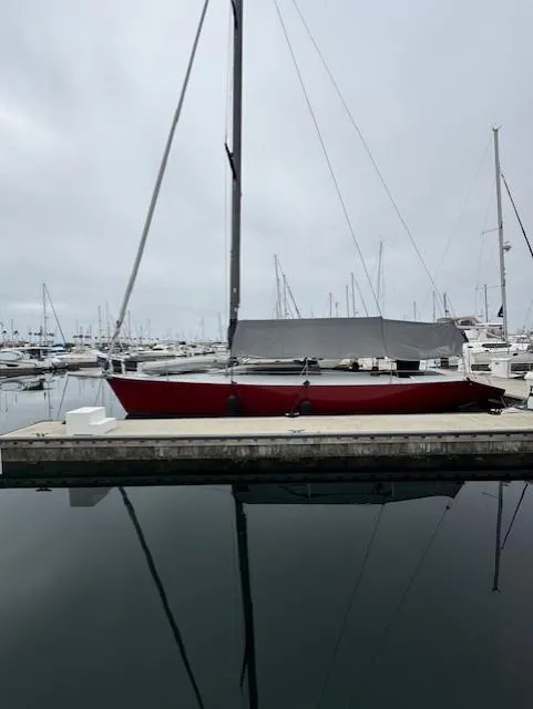 The Image of 1985 Farr PERFORMANCE sailboat docked in a marina, overcast sky reflecting on water. - 0