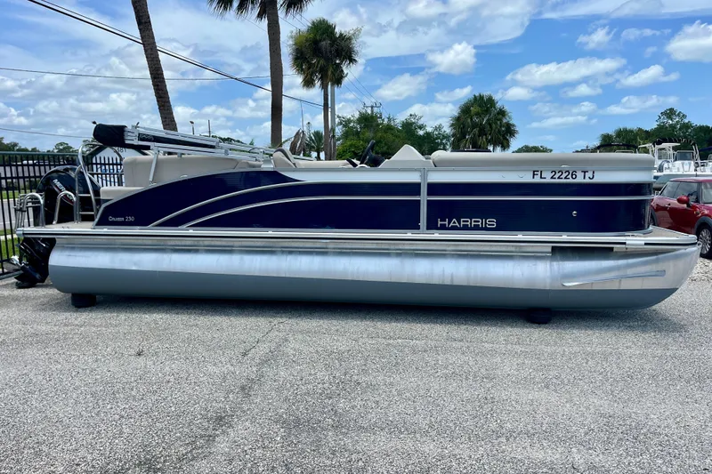 Slide: The Image of 2023 Harris Cruiser 230 pontoon boat parked on pavement under a blue sky. - 3