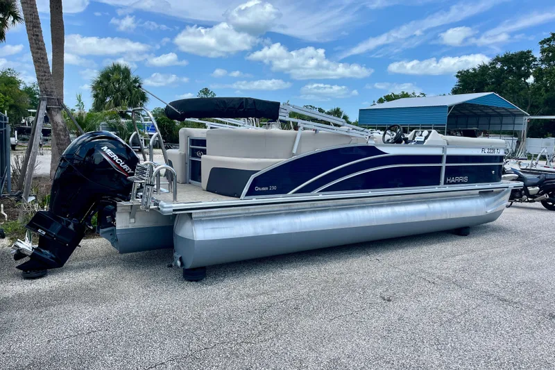 Slide: The Image of 2023 Harris Cruiser 230 pontoon boat with Mercury outboard motor, parked outdoors. - 4