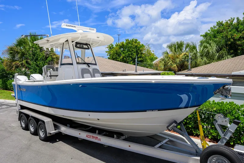 The Image of 2023 Regulator 28 boat on trailer, blue hull, parked outdoors under clear sky. - 0