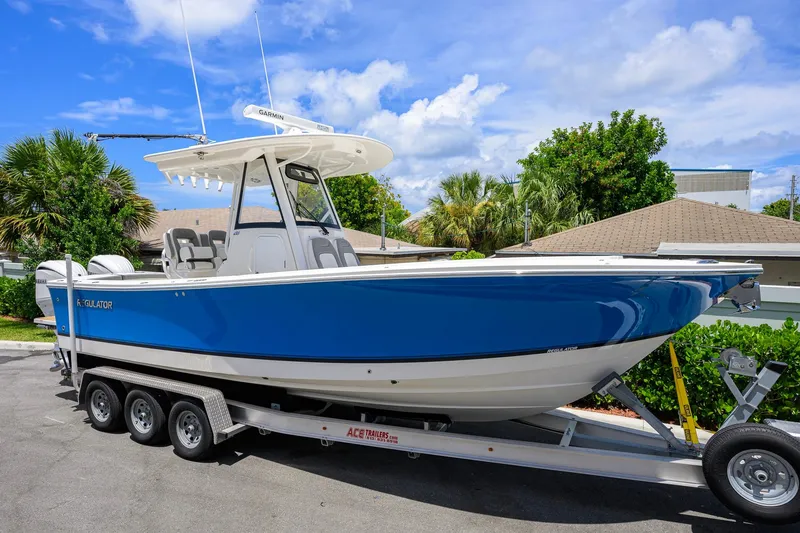 Slide: The Image of 2023 Regulator 28 boat on trailer, blue hull, parked outdoors under a clear sky. - 1