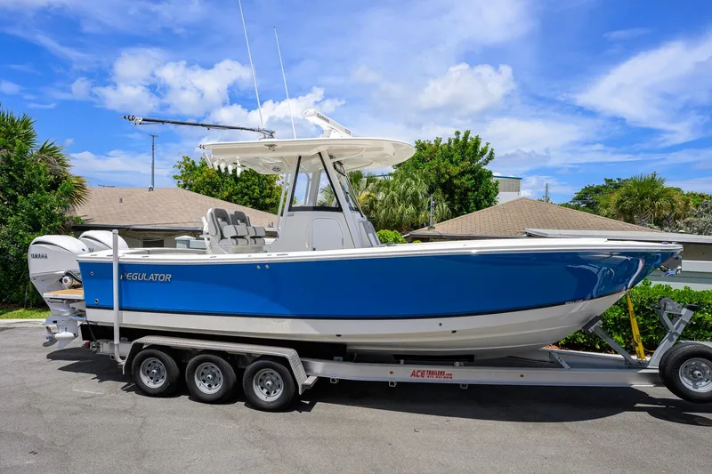 Slide: The Image of 2023 Regulator 28 boat on trailer, blue hull, parked outdoors under clear sky. - 2