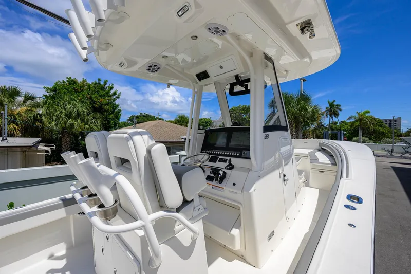 Slide: The Image of 2023 Regulator 28 boat cockpit with dual seats and control panel, surrounded by palm trees. - 28