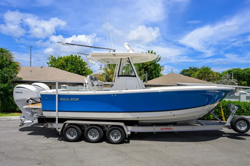 Slide: The Image of 2023 Regulator 28 boat on trailer, blue hull, twin Yamaha engines, sunny day. - 3