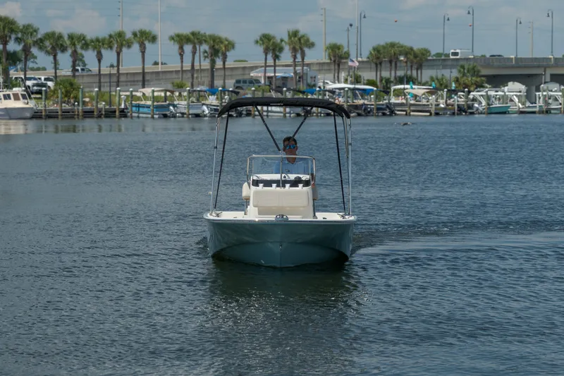 Slide: The Image of A 2027 Boston Whaler 150 Montauk on calm water with a dock in the background. - 7