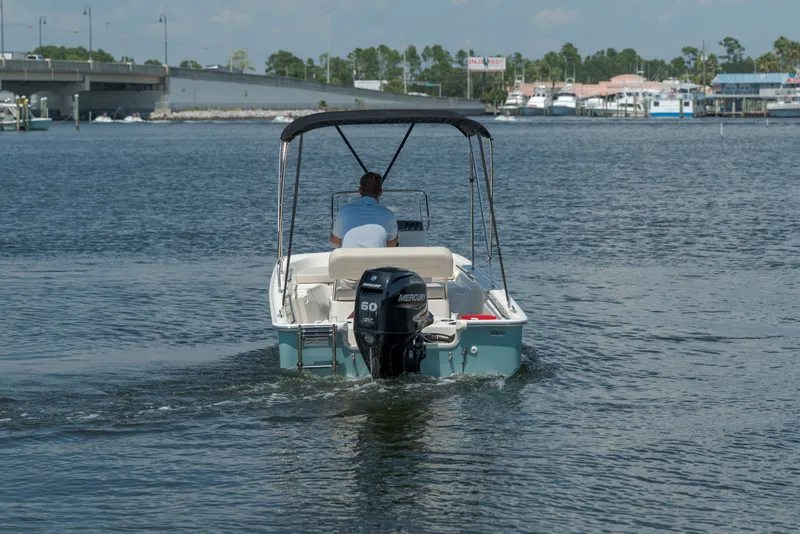 Slide: The Image of A 2027 Boston Whaler 150 Montauk on calm waters. A man is steering the boat. - 2