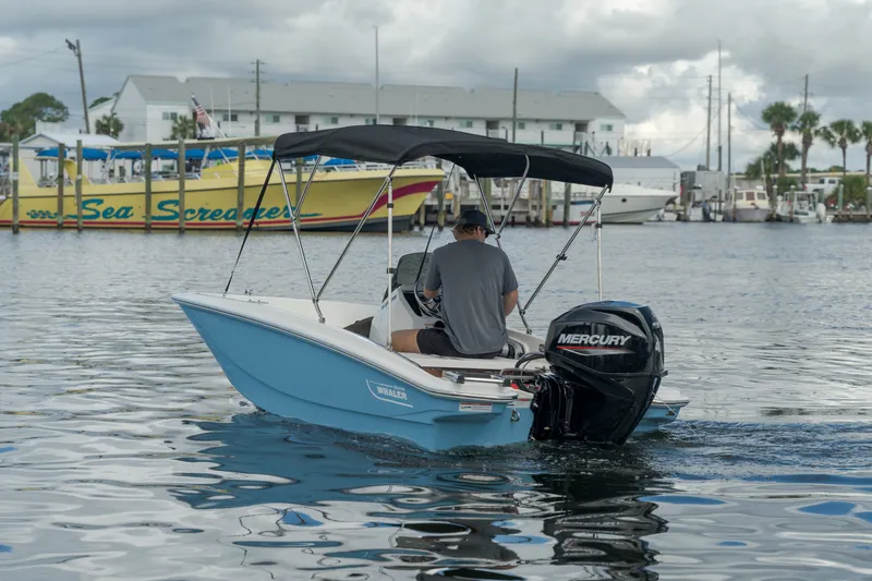 Slide: The Image of A 2027 Boston Whaler 130 Super Sport on calm water. A man is steering the boat. - 1