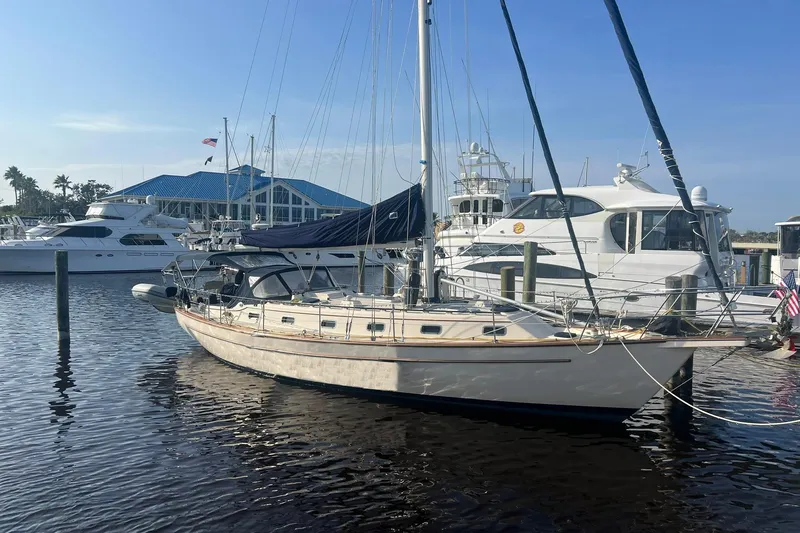 Slide: The Image of 1994 Island Packet 44 cutter sailboat docked at marina with blue-roofed building. - 1