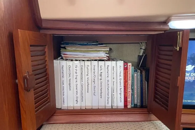Slide: The Image of Open cabinet with organized manuals on a 1994 Island Packet 44 cutter sailboat. - 75