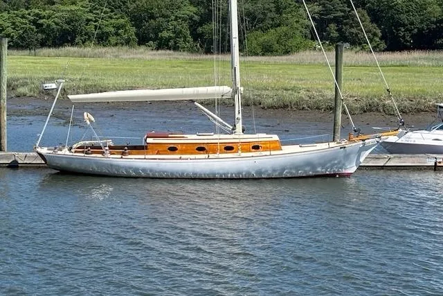 Slide: The Image of Vintage 1979 Nielsen 44 Cutter Rigged sailboat docked by a grassy shoreline. - 2