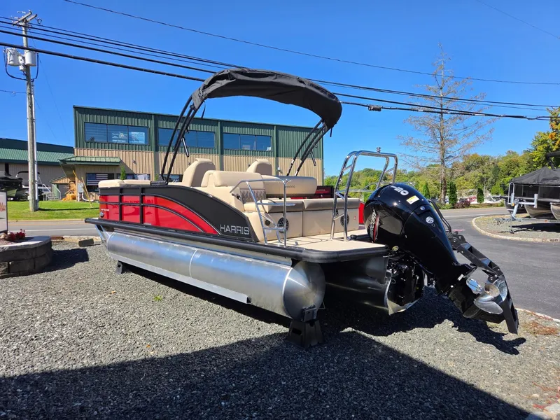 Slide: The Image of 2027 Harris Cruiser 210 pontoon boat with red hull and black bimini top on a gravel lot. - 4