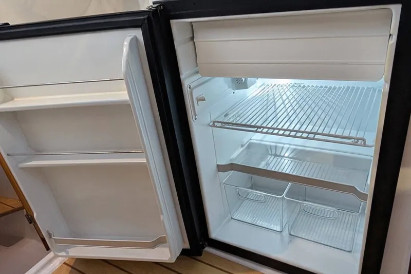 Slide: The Image of Open refrigerator inside a 2017 Cutwater C-24 Coupe boat, showing empty shelves and compartments. - 31