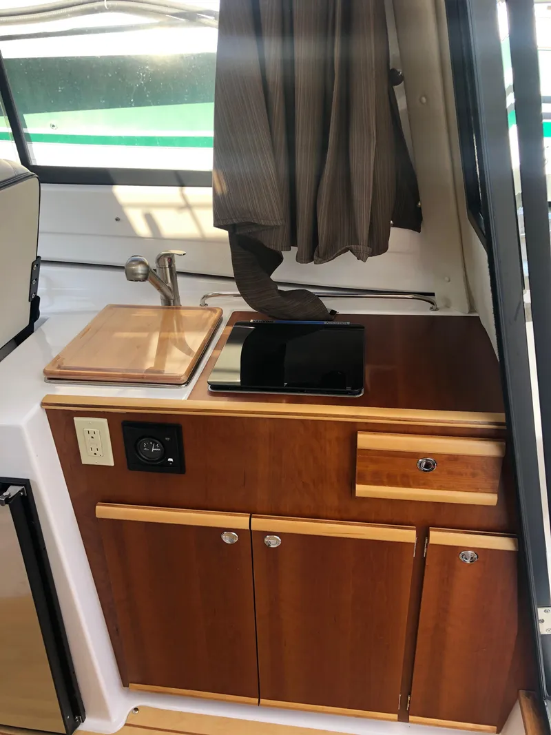 Slide: The Image of Interior of the 2017 Cutwater C-24 Coupe with wooden cabinets, sink, and curtains. - 33