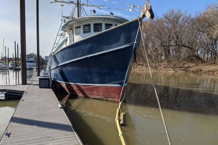 The Image of 1977 Commercial Expedition Trawler docked on a calm river, surrounded by trees and clear skies. - 0