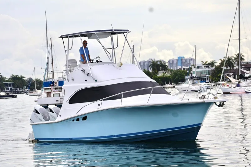 Slide: The Image of 1994 Luhrs 32 Convertible boat cruising in a marina with cityscape background. - 28