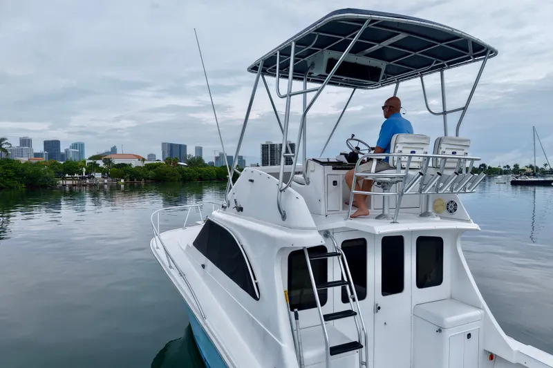 Slide: The Image of 1994 Luhrs 32 Convertible boat with captain, cruising near city skyline. - 33
