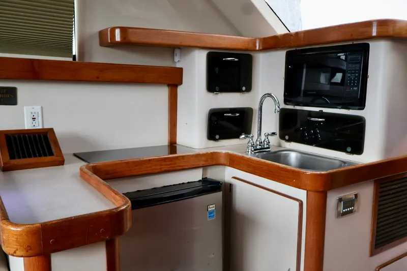 Slide: The Image of 1994 Luhrs 32 Convertible yacht kitchen with sink, microwave, and wooden accents. - 61