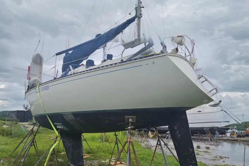The Image of 1986 CNC 29 SL sailboat on stands, undergoing maintenance in a boatyard. - 0