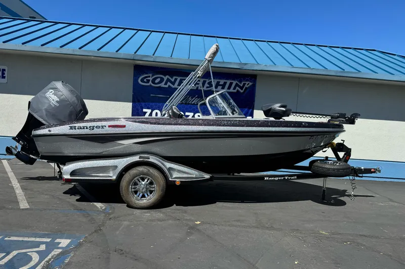 Slide: The Image of 2018 Ranger 1880MS boat on trailer, parked outdoors, with blue building background. - 1