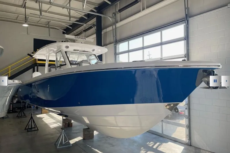 Slide: The Image of 2025 Everglades 395 Center Console boat in a showroom, featuring a sleek blue hull. - 2