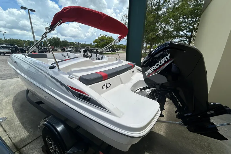 Slide: The Image of 2026 Tahoe T16 boat with Mercury engine, white exterior, red canopy, parked outdoors. - 2
