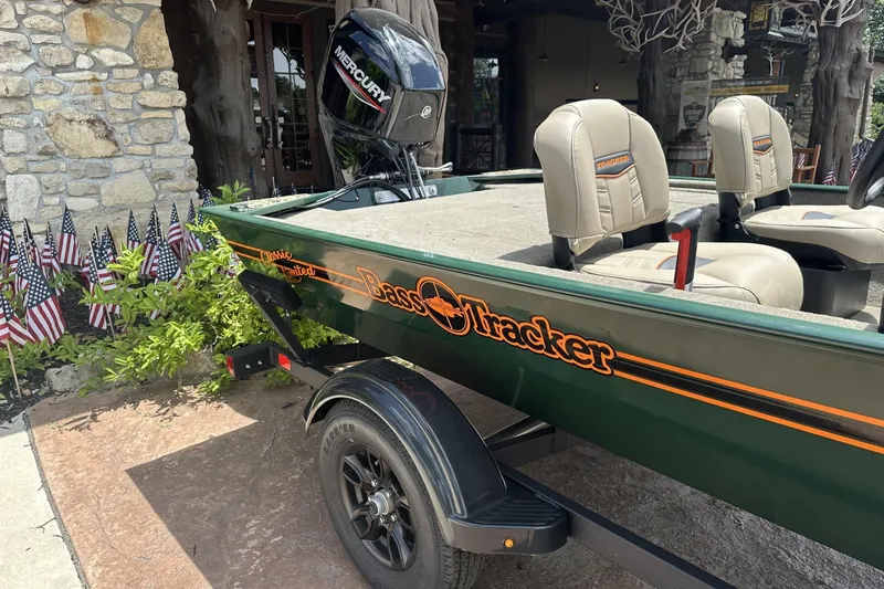 Slide: The Image of 2026 Tracker Bass Tracker Classic Limited boat with Mercury engine, parked near American flags. - 4