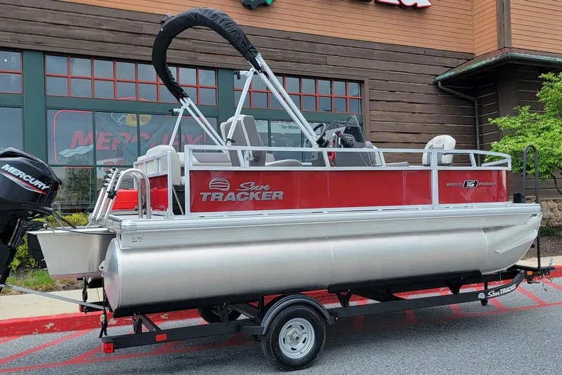 The Image of 2026 Sun Tracker Bass Buggy 16 XL Select pontoon boat on trailer, parked outside a building. - 0
