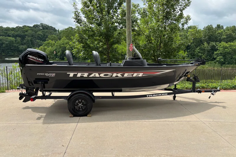 The Image of 2026 Tracker Pro Guide V-16 SC boat on trailer, parked near a scenic lake. - 0