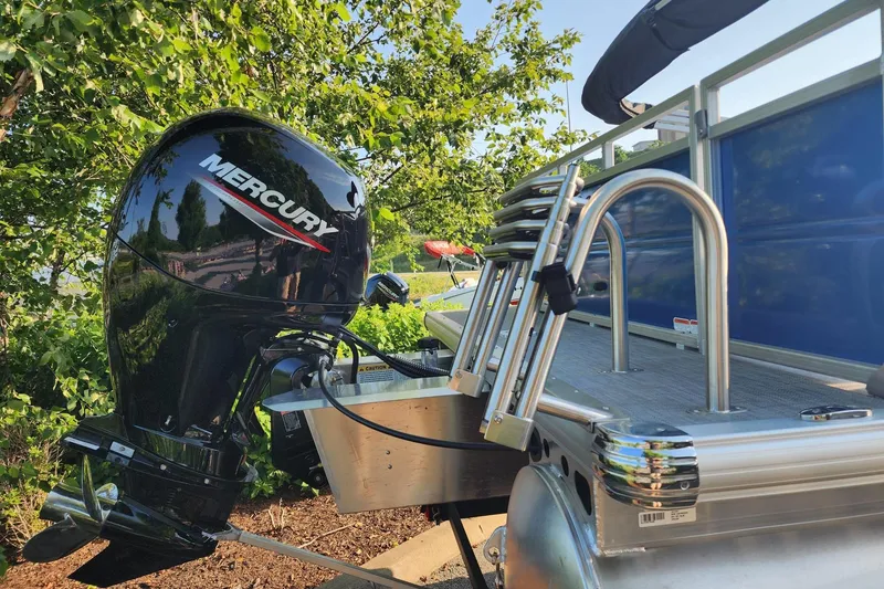 Slide: The Image of 2026 Sun Tracker Party Barge 22 RF DLX with Mercury outboard motor, docked near lush greenery. - 2