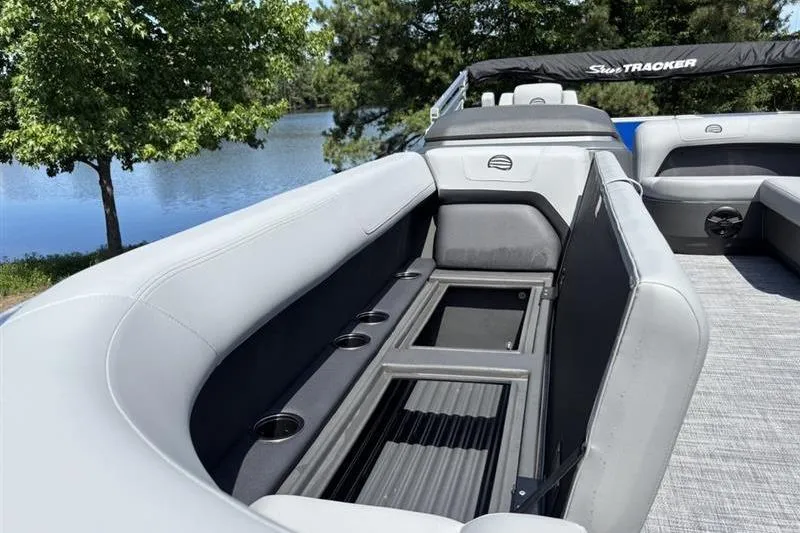 Slide: The Image of 2026 Sun Tracker Party Barge 18 DLX interior with seating and cup holders by a lake. - 10