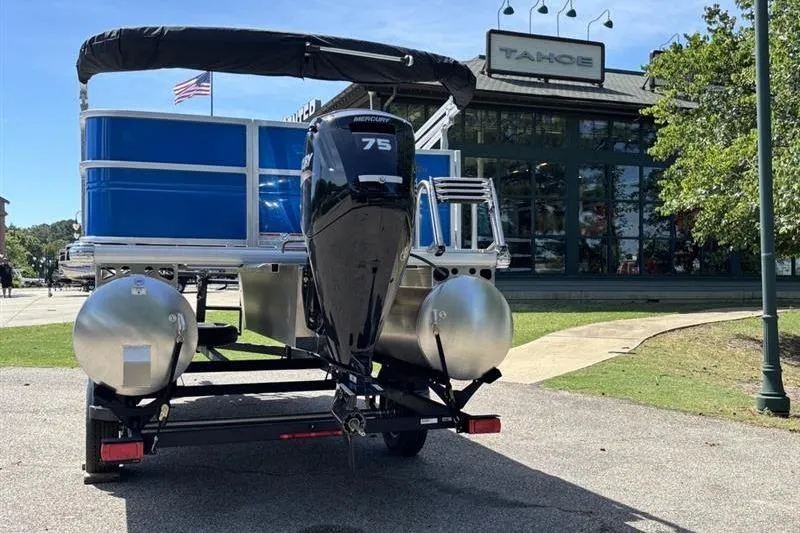Slide: The Image of 2026 Sun Tracker Party Barge 18 DLX on trailer, parked near a building. - 2