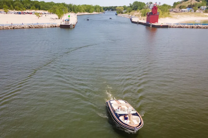 Slide: The Image of 2022 Chris Craft 34 Launch Heritage boat cruising near a red lighthouse and sandy beach. - 11