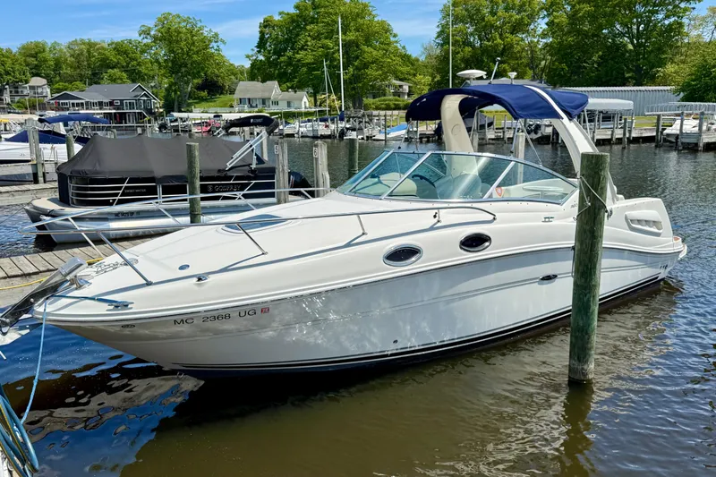 Slide: The Image of 2005 Sea Ray Sundancer 260 docked at a marina, surrounded by calm water and greenery. - 2