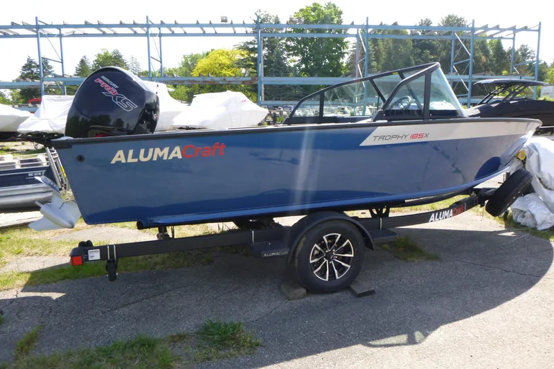 The Image of 2025 Alumacraft Trophy 185X Sport boat on trailer, blue exterior, parked outdoors. - 1