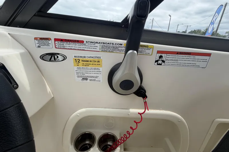 Slide: The Image of 2023 Stingray 231 DC boat dashboard with throttle, warning labels, and cup holders. - 27