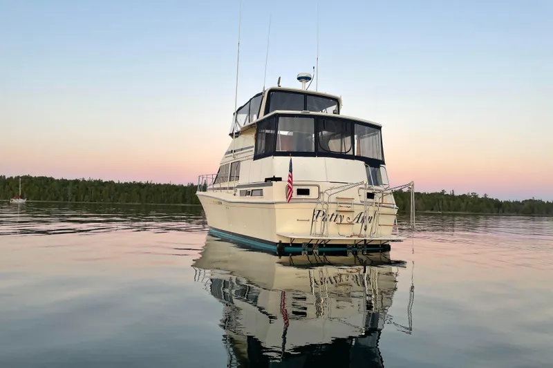Slide: The Image of 1987 Chris-Craft 427 Catalina yacht on calm water at sunset, reflecting serene surroundings. - 4