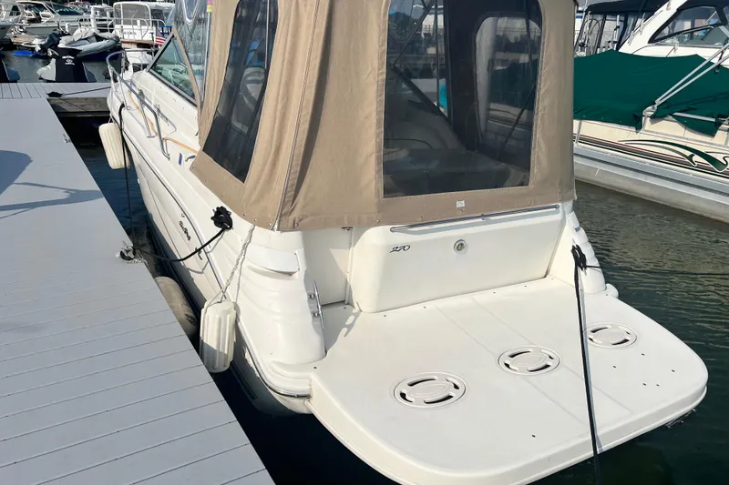 The Image of 1997 Sea Ray 270 Sundancer docked at marina, featuring beige canopy and spacious swim platform. - 0
