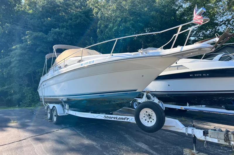 Slide: The Image of 1997 Sea Ray 270 Sundancer boat on trailer, parked outdoors with trees in background. - 3