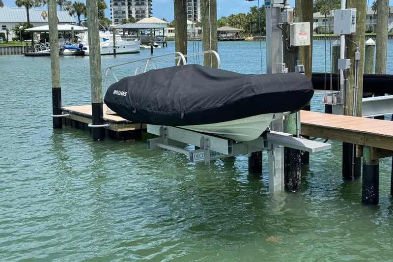 Slide: The Image of 2025 Williams Jet Tenders Sportjet 345 covered on a dock lift by the water. - 16