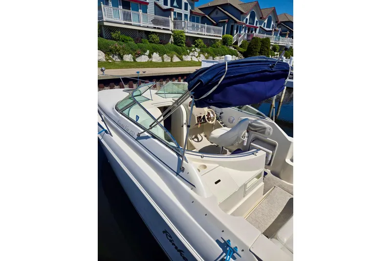 Slide: The Image of 1999 Rinker Fiesta Vee 270 boat docked near waterfront homes, featuring a blue canopy. - 2