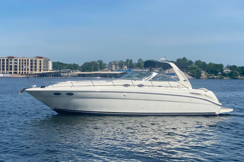 Slide: The Image of 2004 Sea Ray 380 Sundancer yacht on calm water, with buildings and trees in the background. - 2