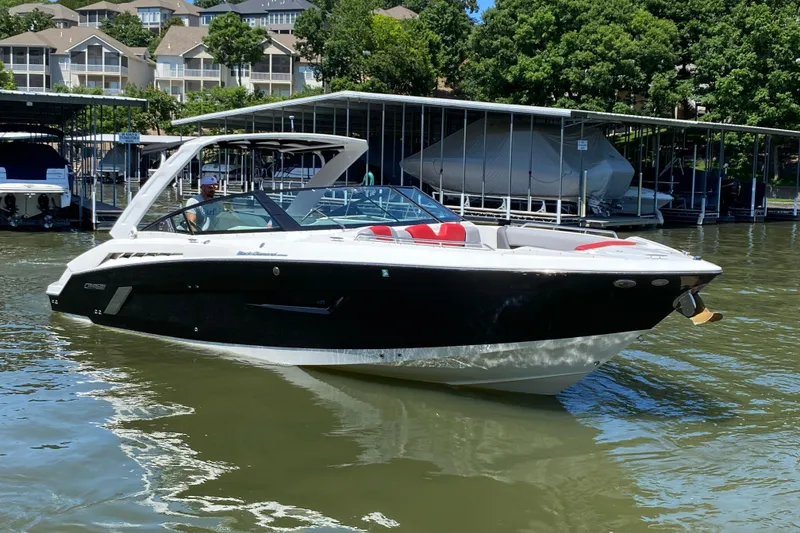 Slide: The Image of 2014 Cruisers Sport Series 328 Black Diamond boat on water near docks and trees. - 1